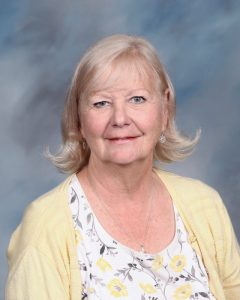 Older woman in yellow cardigan smiling against blue background