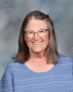 Smiling older woman with glasses wearing blue sweater against blurry background