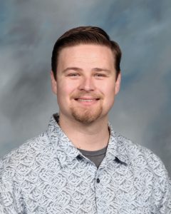 Smiling person in patterned button-up shirt against blurred background