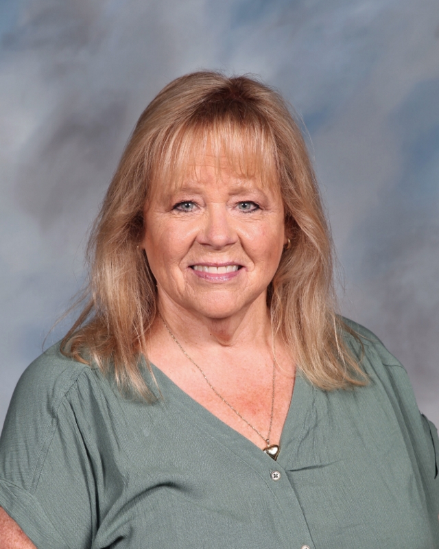 Smiling woman in green top against blurry background, professional headshot
