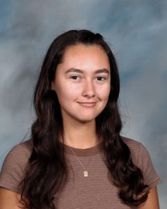 Smiling student with long dark hair wearing striped shirt against blue background