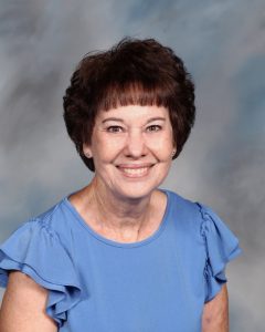 Smiling person in blue top with curly hair against mottled background