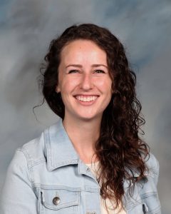 Smiling woman with long curly hair wearing light denim jacket