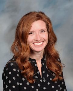 Smiling woman with wavy red hair wearing polka dot black shirt