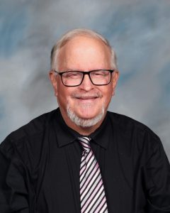 Smiling older person with glasses and a striped tie in professional headshot