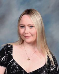 Woman with blonde hair smiling in a black patterned blouse