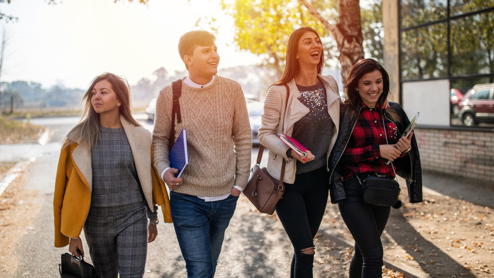 Four students walking together on autumn street, smiling and carrying books