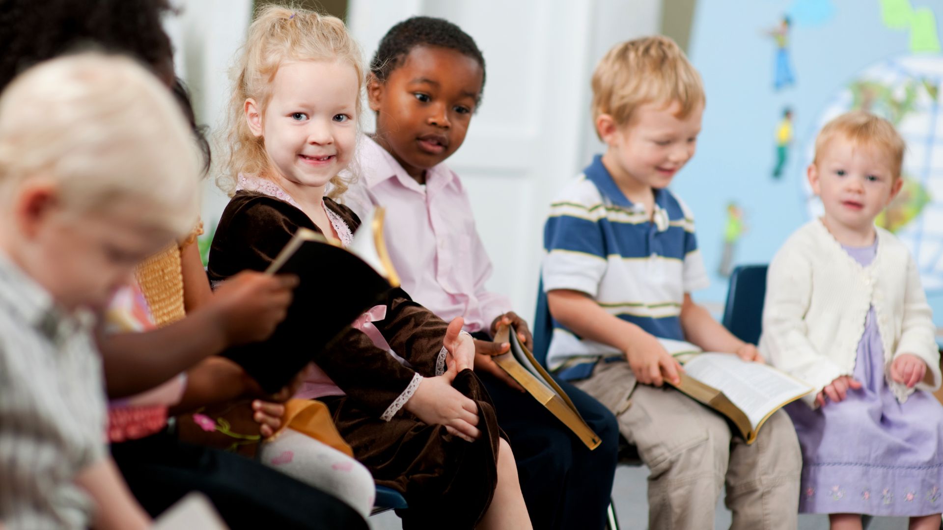 Diverse group of young children reading books together in classroom
