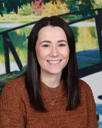 Smiling person in brown sweater sitting near a colorful background