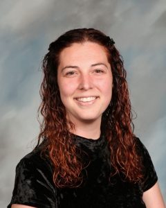 Smiling person with curly reddish-brown hair in black shirt